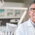 a confident, professional implant surgeon, poised in a modern, well-lit clinic, examines state-of-the-art dental tools against a backdrop of sleek, sterile surroundings, embodying expertise and precision.