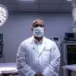 a focused implant surgeon, clad in a crisp white coat and mask, stands confidently in a state-of-the-art operating room, illuminated by bright, sterile lights, showcasing the precision and expertise that distinguishes the best in the field.