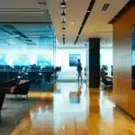 a sleek, modern office workspace features a polished wooden desk centered against a backdrop of glass walls showcasing a bustling city skyline, illuminated by vibrant artificial lighting, creating an ambiance of innovation and professionalism.