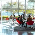 a sleek, modern office space with floor-to-ceiling glass walls showcases a diverse team engaged in a dynamic brainstorming session, illuminated by bold color accents and vibrant digital displays.