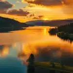 a breathtaking sunset casts golden hues over a serene lake, reflecting vibrant colors on the tranquil water surface surrounded by lush greenery.