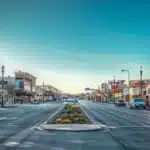 a bustling urban street in lake worth, texas, showcasing a modern extraction office with a large, bold sign announcing affordable extraction services, surrounded by vibrant storefronts and a clear blue sky.