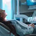 a modern dental office featuring a patient discussing oral hygiene techniques with a dentist, illuminated by bright overhead lights, showcasing dental implants prominently on a sleek digital display, emphasizing the connection between dental health and breath freshness.