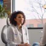 a well-lit dental office showcases a confident patient seated in a modern dental chair, discussing the advantages of choosing dentures with a knowledgeable dentist, surrounded by advanced dental equipment and informative brochures.