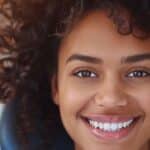 a close-up shot of a confident individual smiling brightly in a sleek, modern dental office, showcasing the seamless integration of dental implants and emphasizing a natural, convincing appearance.