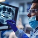 a focused periodontist in a modern dental clinic diligently examines a patient's dental x-rays on a sleek digital screen, showcasing advanced technology in oral health care.