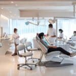 a modern dental clinic boasts a sleek, sterile environment with high-tech equipment and a patient reclining in a plush chair, surrounded by attentive dental professionals preparing for an intricate implant procedure, underscored by soft, clinical lighting.