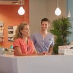 a modern dental clinic reception in mansfield, texas, featuring sleek furnishings and bright lighting, where a welcoming staff member assists a diverse group of patients exploring affordable denture and implant options.
