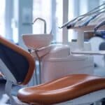 a polished dental clinic setting features a gleaming dental chair and a set of lifelike dentures displayed prominently on a sleek counter, highlighting their role as a popular dental replacement.