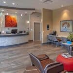 a modern dental clinic reception in mansfield, texas, featuring a warm, inviting atmosphere with sleek furniture and vibrant dental posters, showcasing a display of affordable dentures prominently on a stylish counter.