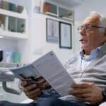 a concerned older adult sits in a modern dental clinic, analyzing an informative brochure about dentures, with clinical tools and a dental chair subtly visible in the background.