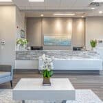 a modern dental clinic reception area in mansfield, texas, showcasing a welcoming atmosphere with sleek furniture, bright overhead lighting, and promotional materials highlighting affordable dentures and implants.
