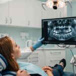 a detailed close-up of a modern dental office, featuring a patient in a sleek chair looking concerned, with a dental professional analyzing a digital x-ray displaying bone loss and implants on a high-tech monitor, surrounded by sophisticated dental equipment and ambient led lighting.